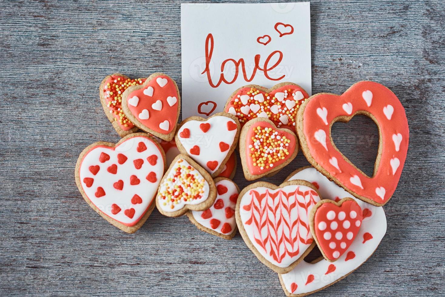 Decorated and glazed heart shape cookies and paper note with inscription LOVE on the gray background, top view. Valentines day concept photo