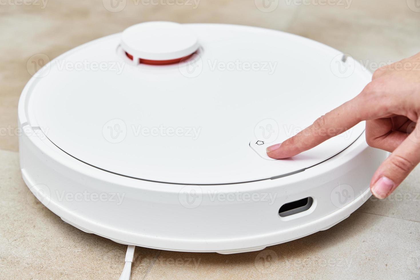 Hand push start button on robot vacuum cleaner. Modern smart household photo