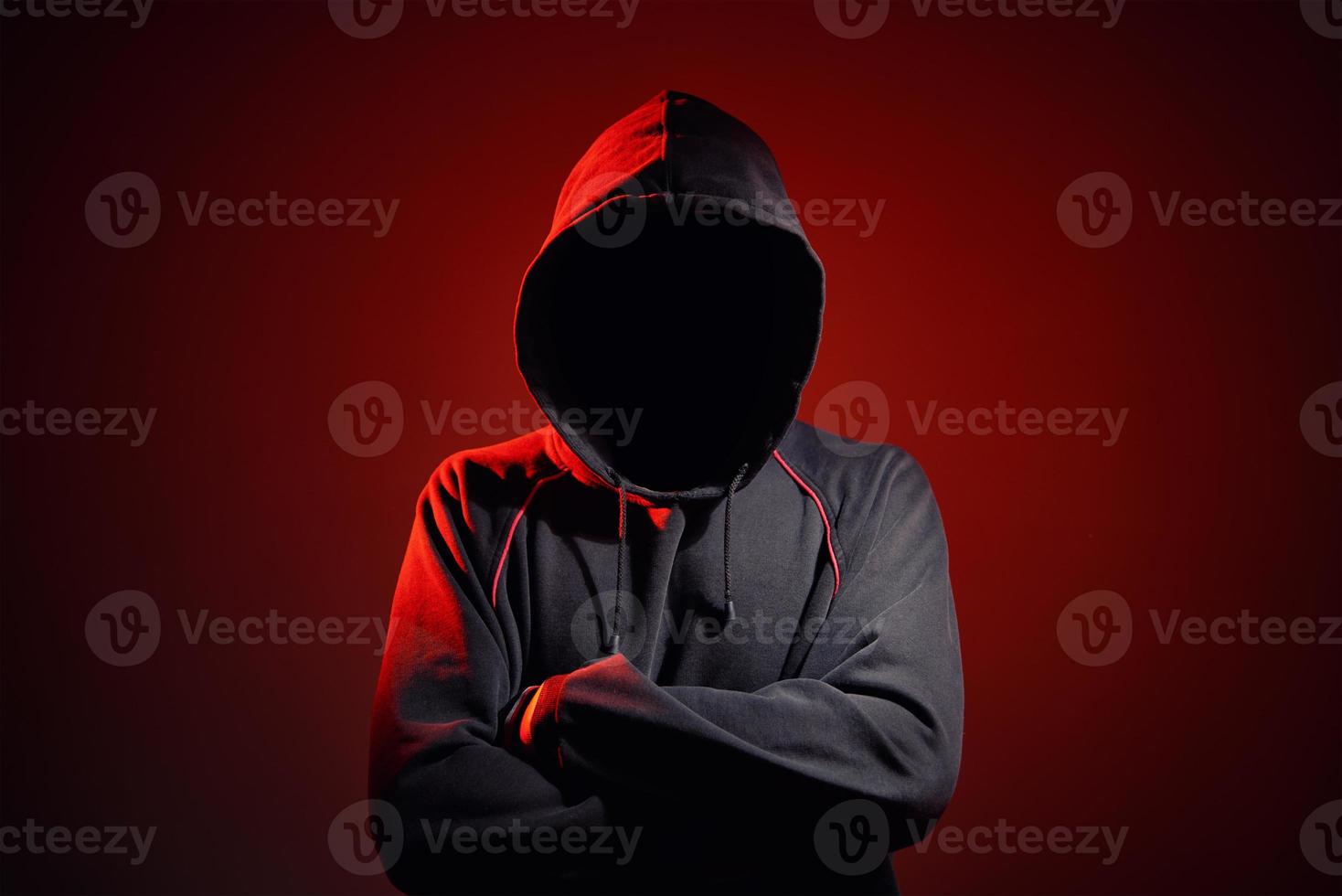 Silhouette af man without face in hood on red background. Anonymous crime photo