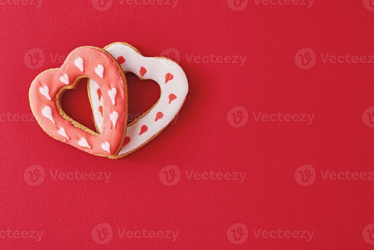 Two decorated with icing and glazed heart shape cookies on the red background with copy space. Valentines Day food concept photo