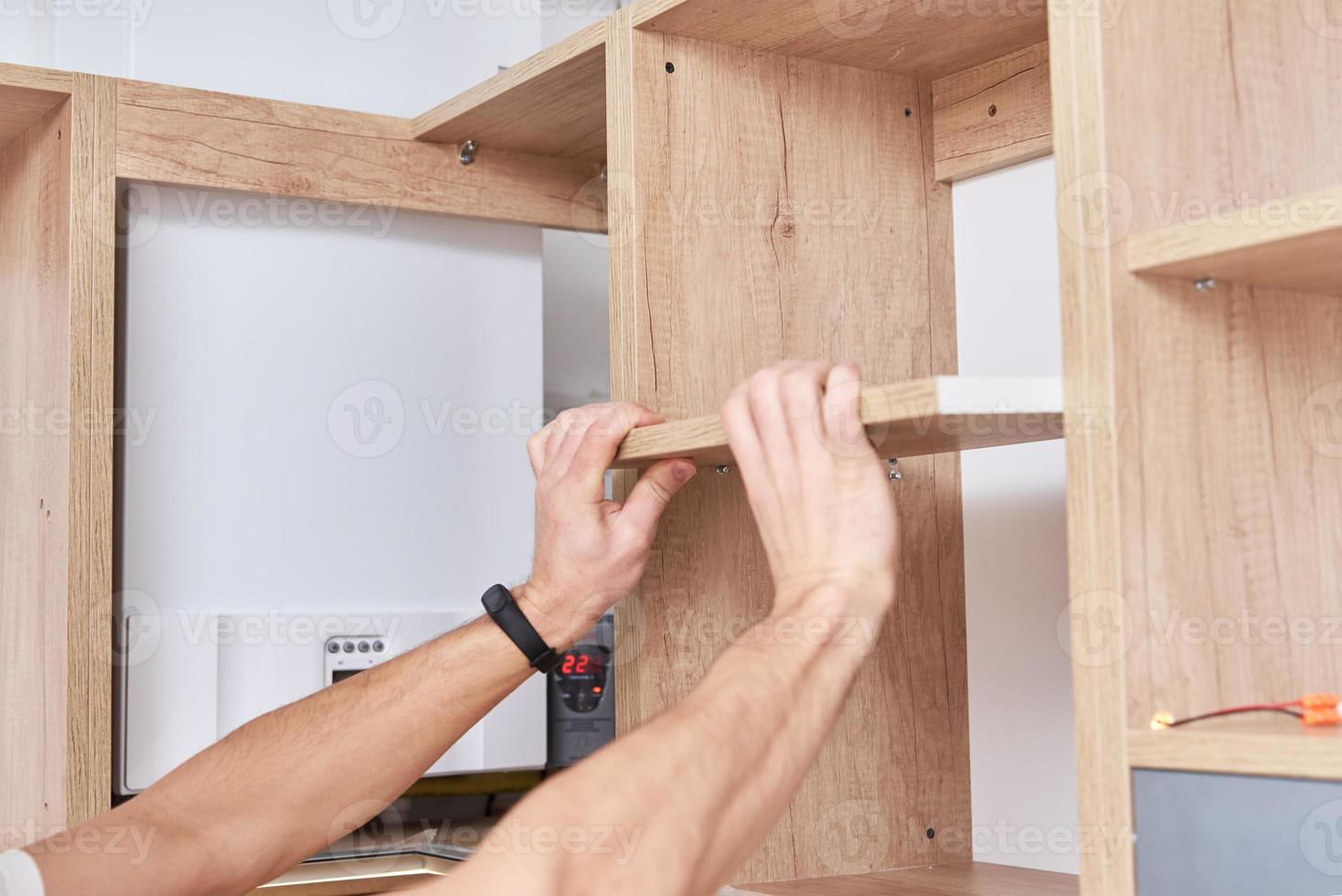 Male carpenter install shelf in kitchen cabinet photo