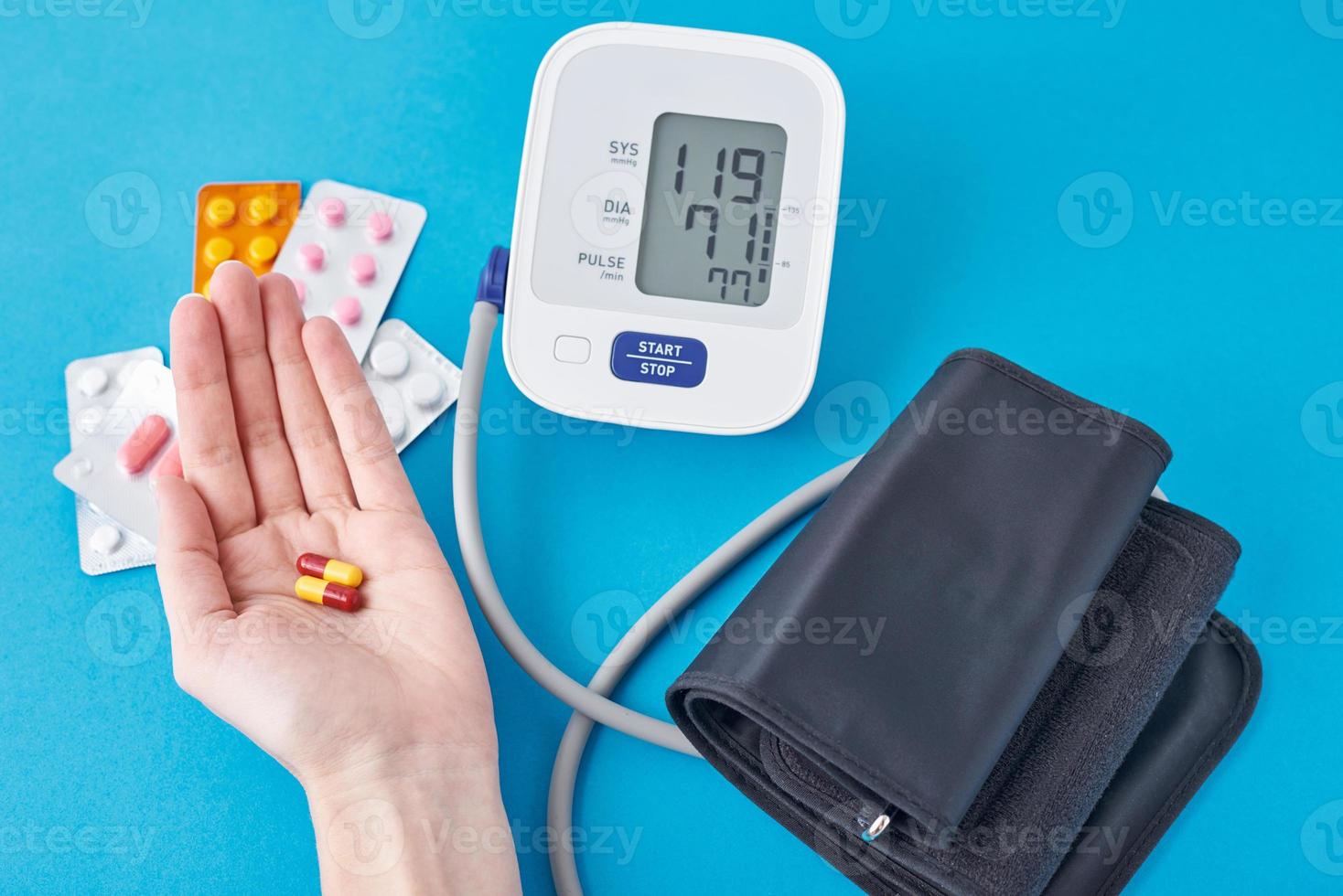 Digital blood pressure monitor and medical pills in hand on a blue background. Healthcare and medicine concept photo