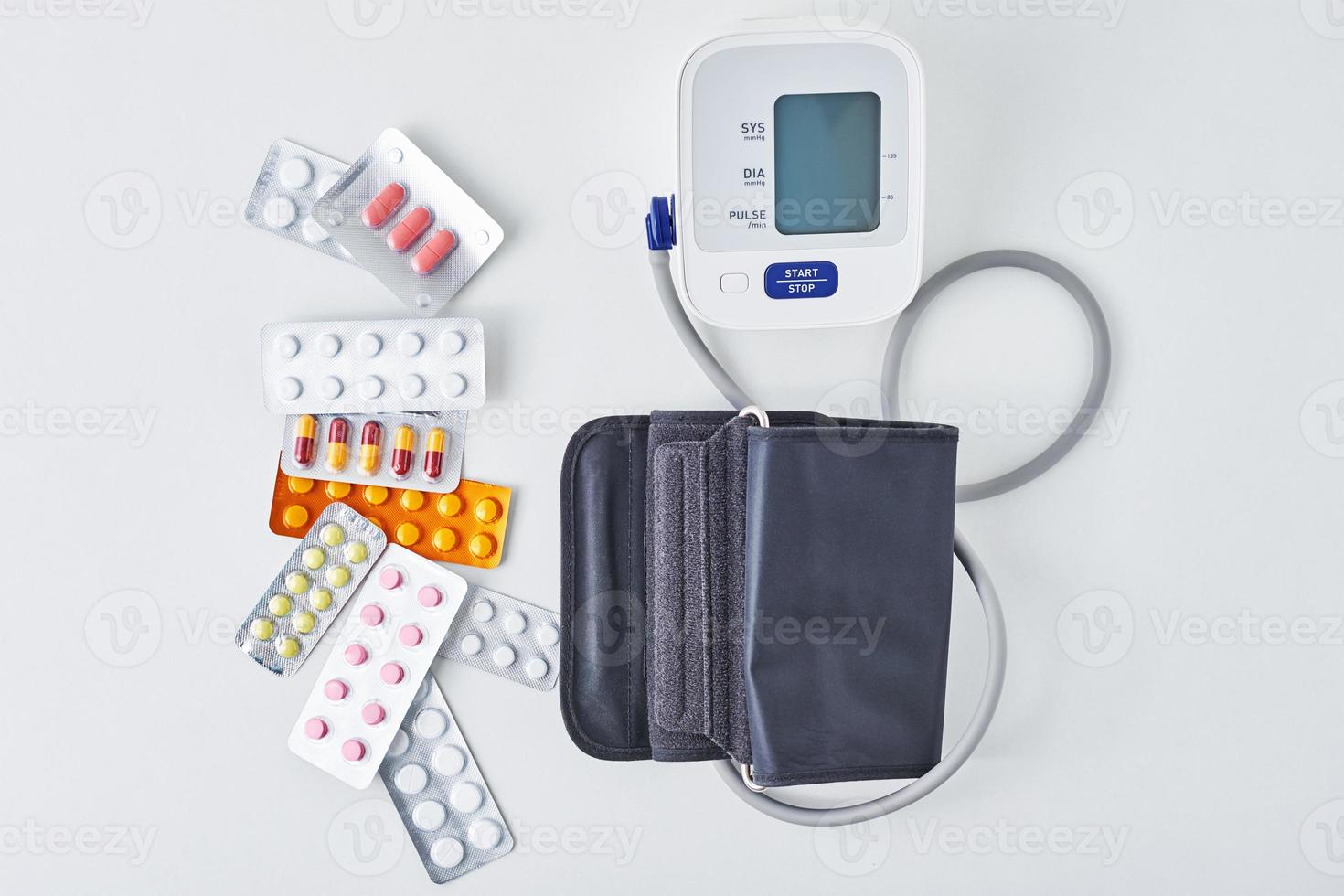 Digital blood pressure monitor and medical pills on the white table. Healthcare and medicine concept photo