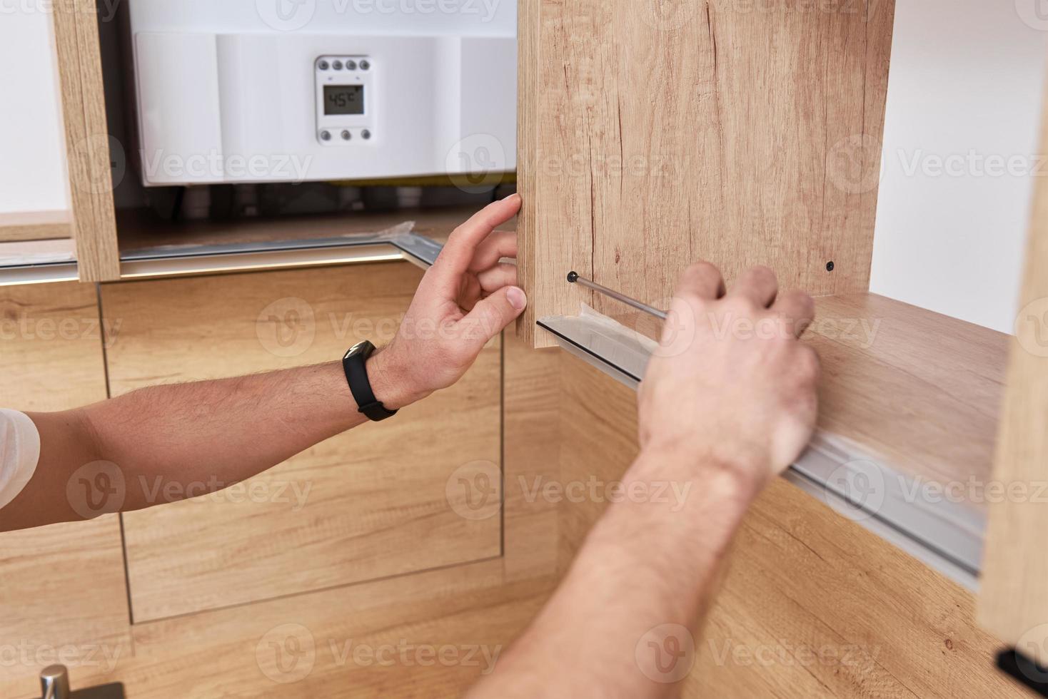 Male carpenter install shelf in kitchen cabinet photo