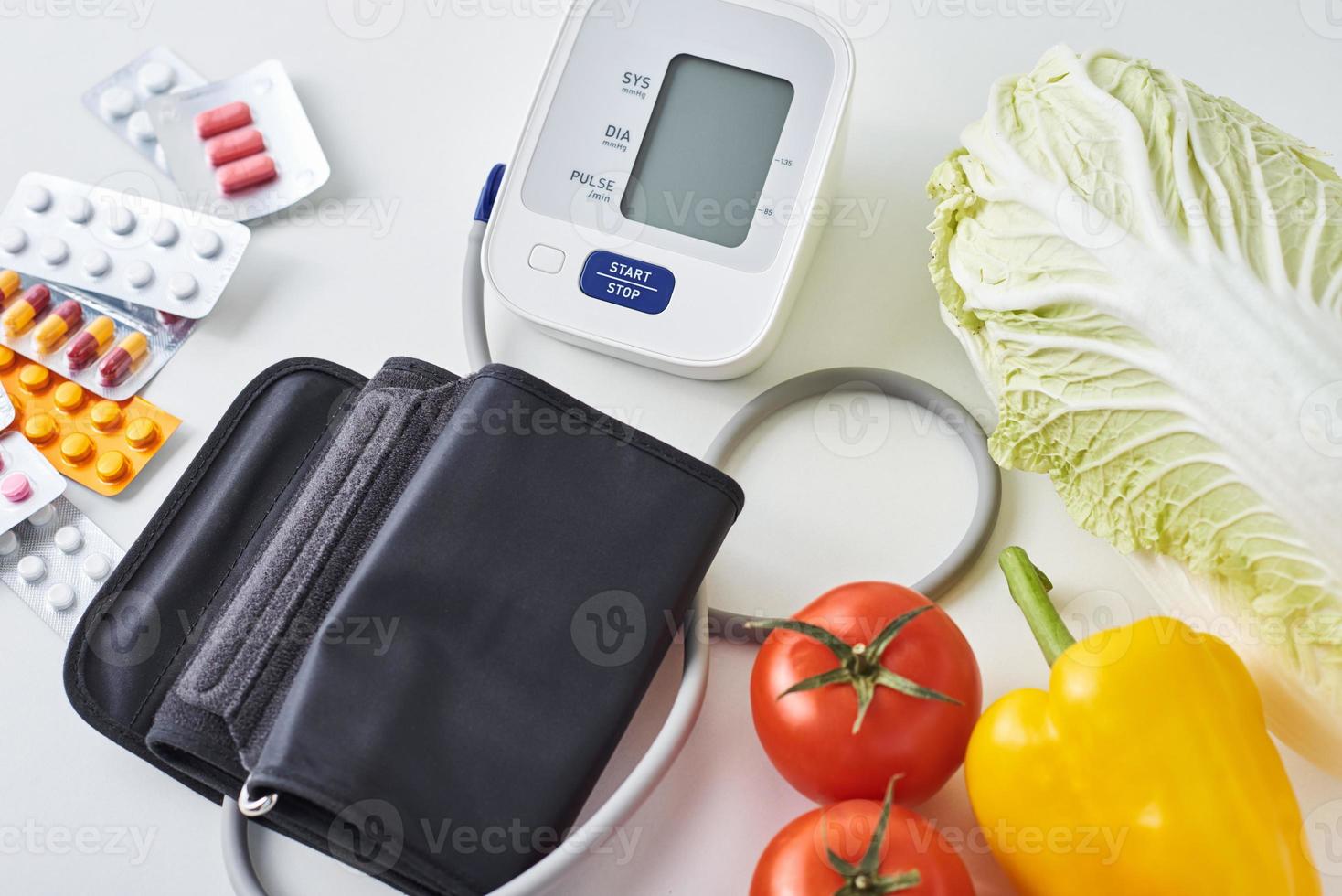 Digital blood pressure monitor, fresh vegetables and medical pills on a white background. Healthy lifestyle concept photo