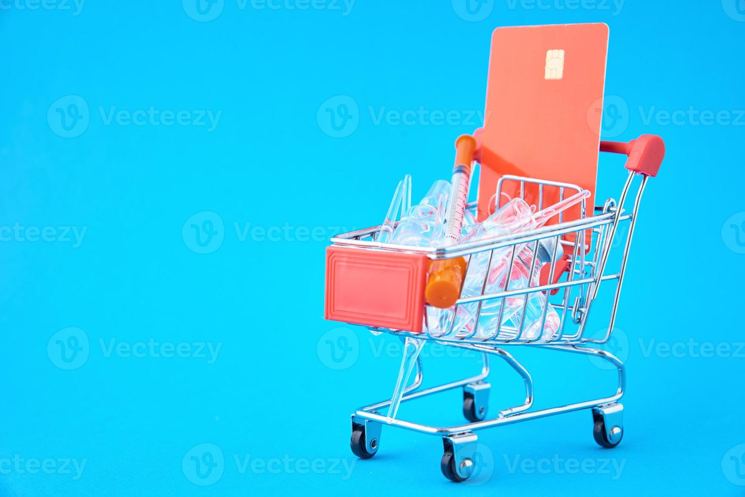 Syringes and ampoules with medicine in shopping cart on blue background photo