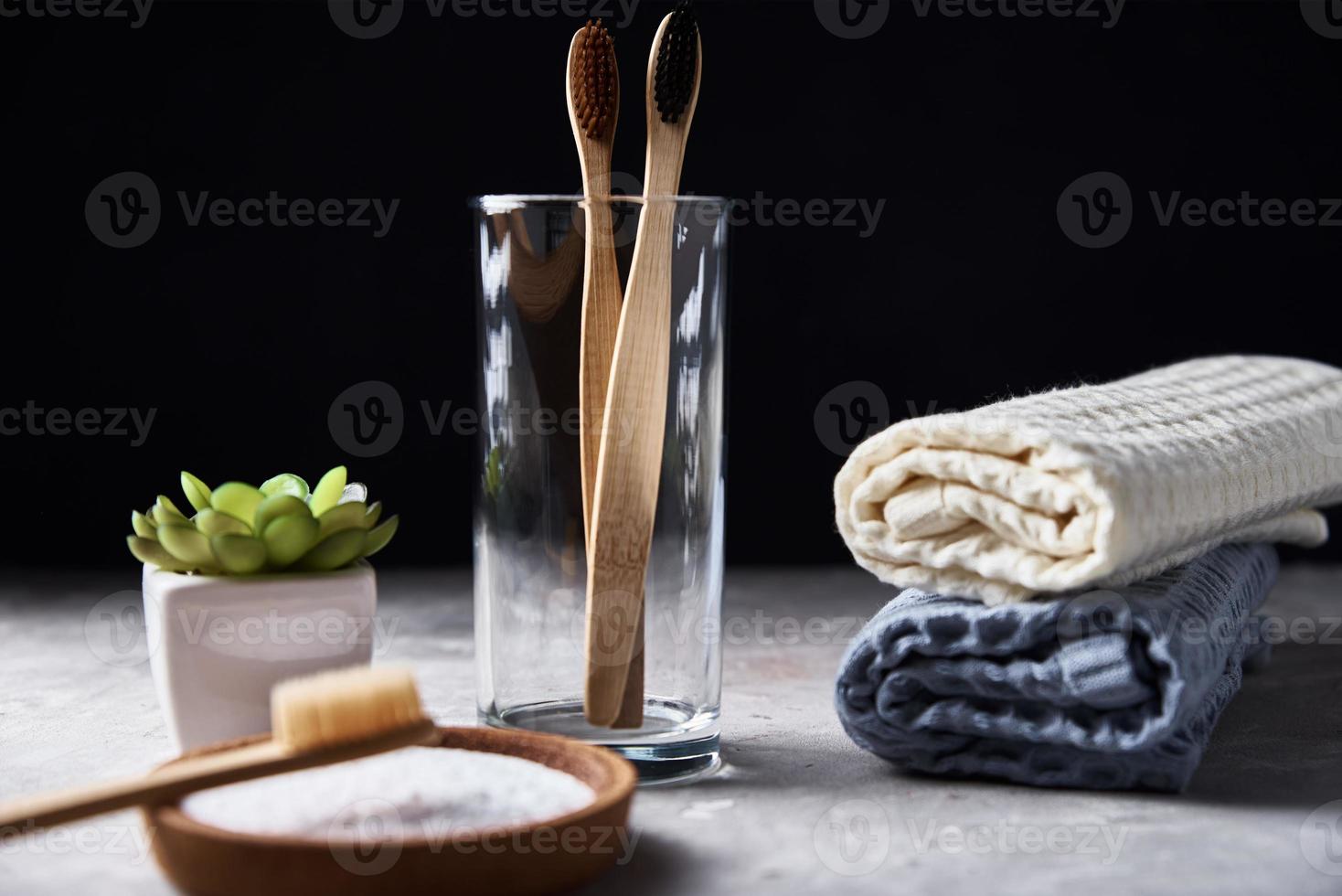 Bamboo toothbrushes in glass and bathroom towels on dark background photo