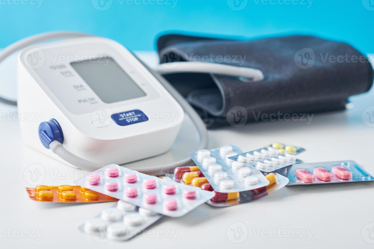 Digital blood pressure monitor and medical pills on the white table. Healthcare and medicine concept photo