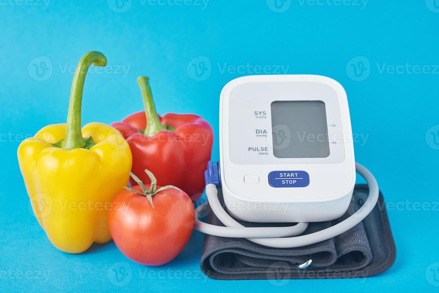 Digital blood pressure monitor and fresh vegetables on a blue background. Healthcare concept photo