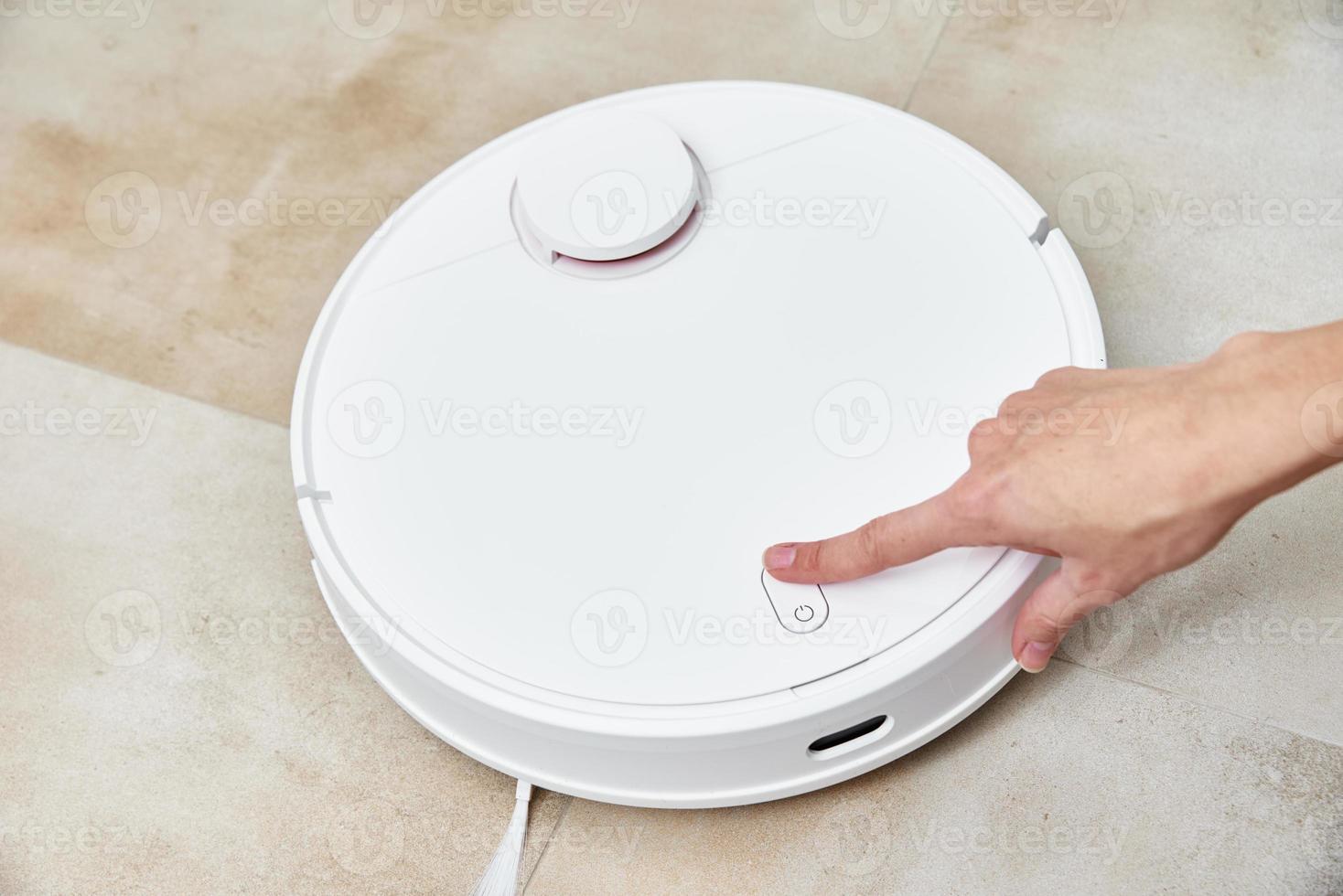 Hand push start button on robot vacuum cleaner. Modern smart household photo