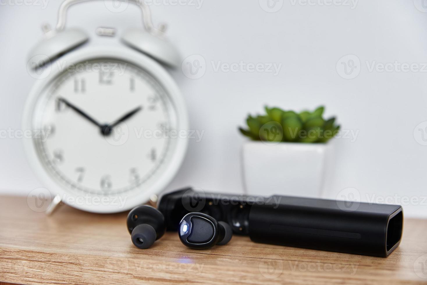 Wireless earphones on shelf with alarm clock and house plant. photo