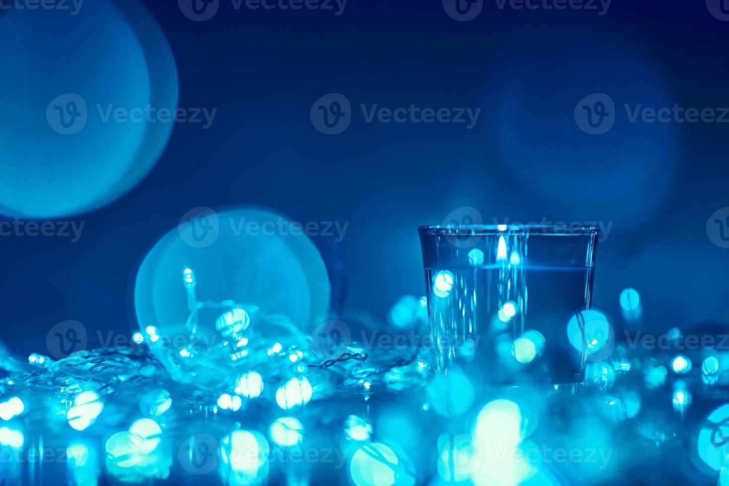 Silhouette of burning candle with a golden blurred lights on dark background, blue toned photo