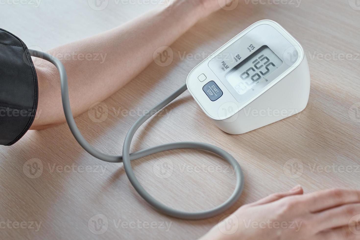 Woman measuring blood pressure with a digital pressure monitor against blue background. Health care and medical concept photo