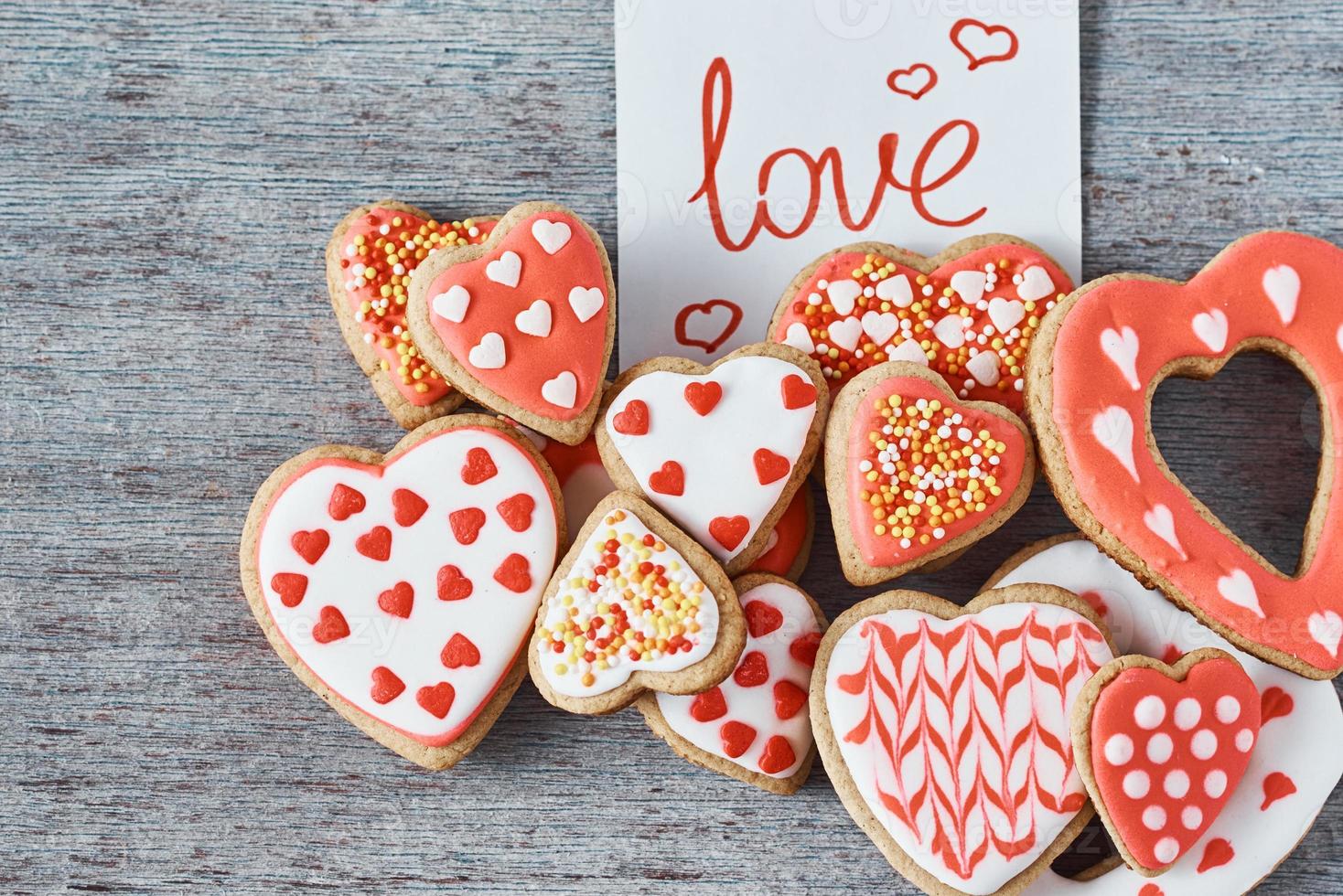 Decorated and glazed heart shape cookies and paper note with inscription LOVE on the gray background, top view. Valentines day concept photo