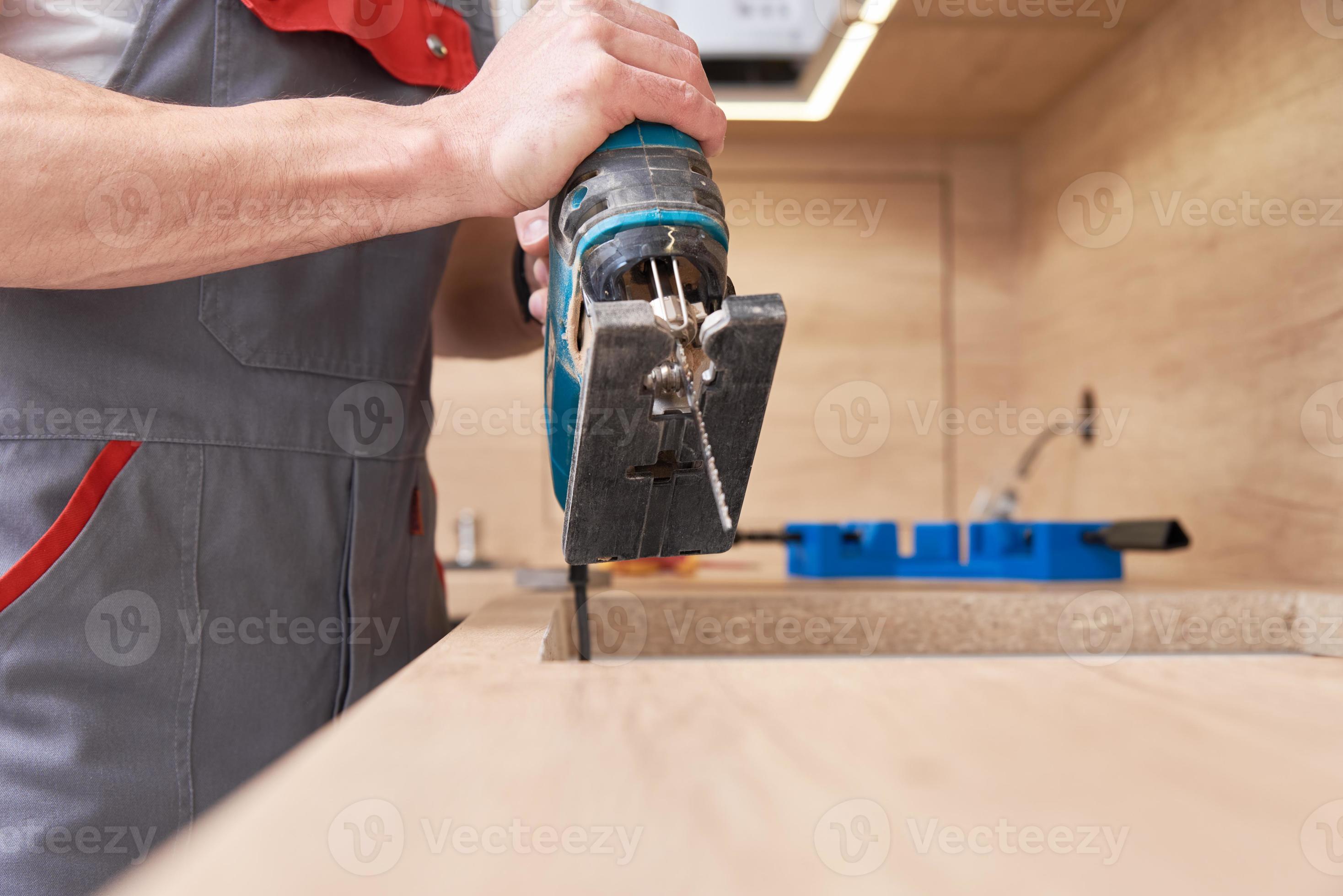 Repairman using electric jigsaw. Sawing place for installing gas hob in