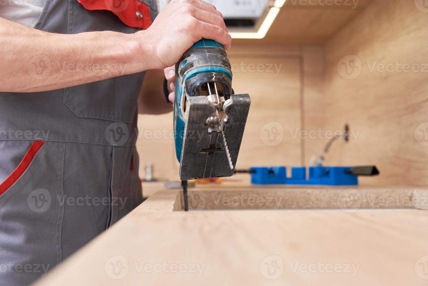 Repairman using electric jigsaw. Sawing place for installing gas hob in worktop photo