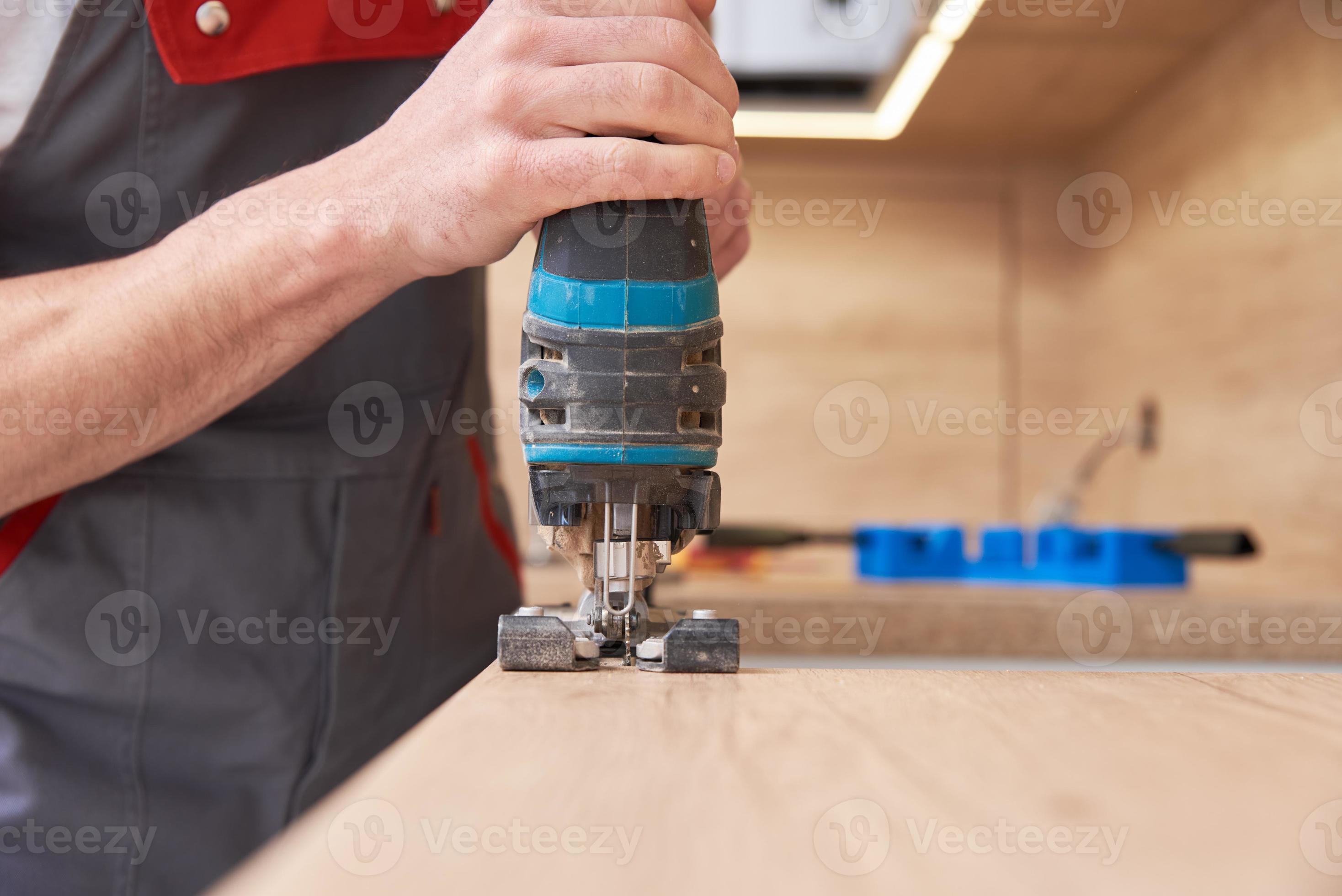 Repairman using electric jigsaw. Sawing place for installing gas hob in