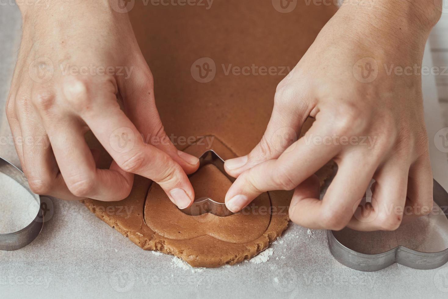 hacer galletas de jengibre en forma de corazón para el día de san valentín. cortador de galletas de uso de mano de mujer. concepto de comida navideña foto