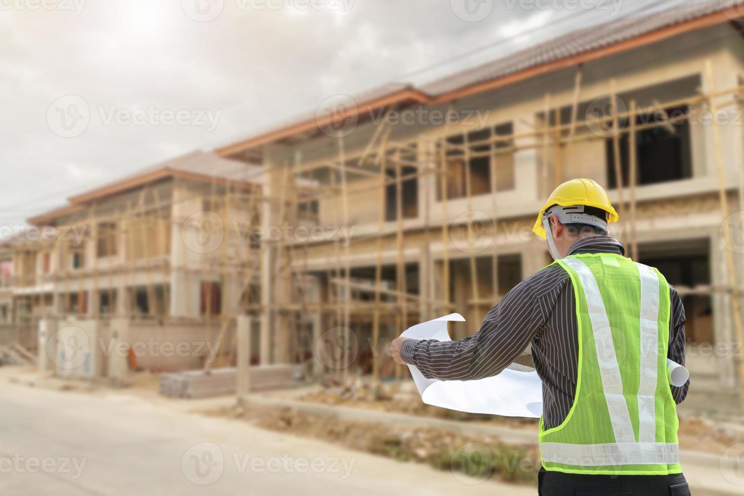 young professional engineer in protective helmet and blueprints paper at the house building construction site photo