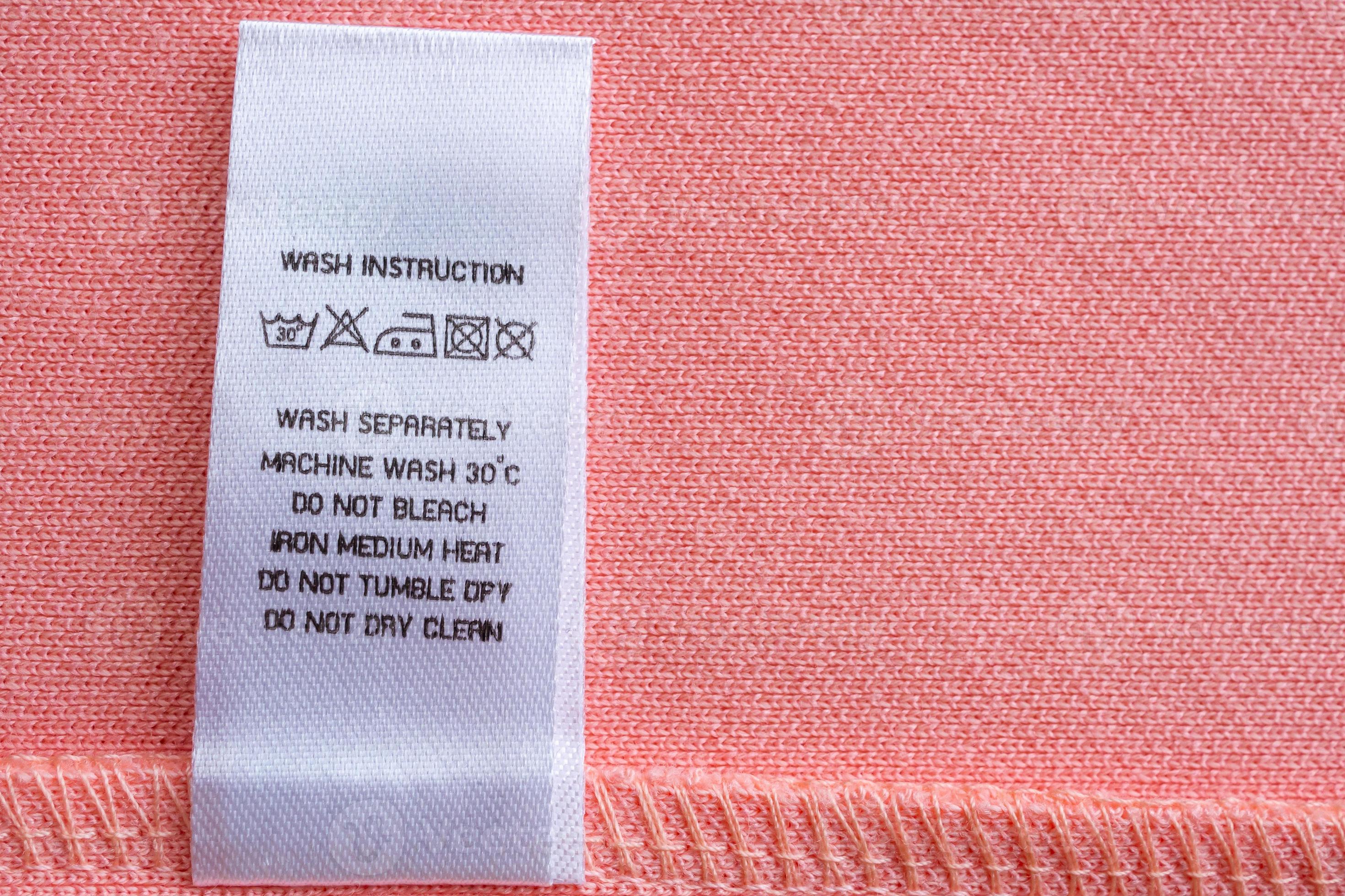 https://static.vecteezy.com/system/resources/previews/013/053/142/large_2x/white-laundry-care-washing-instructions-clothes-label-on-pink-cotton-shirt-photo.jpg