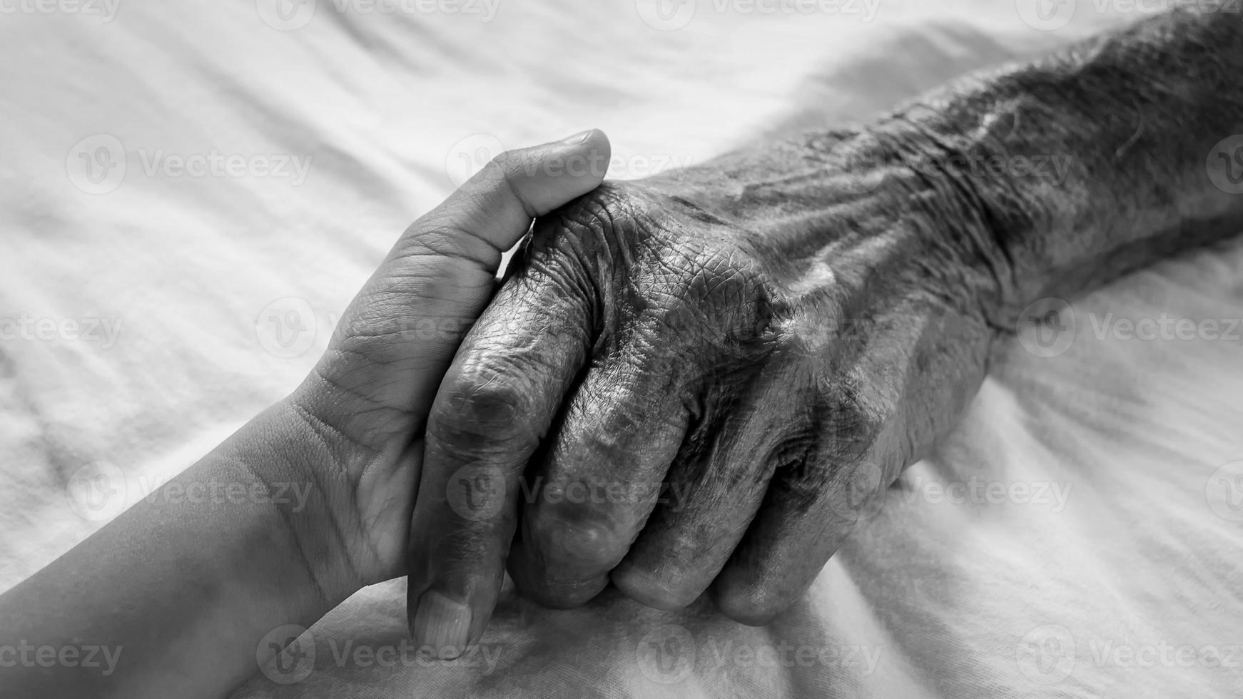 Hands of the old man and a child's hand on the white bed in a hospital. photo