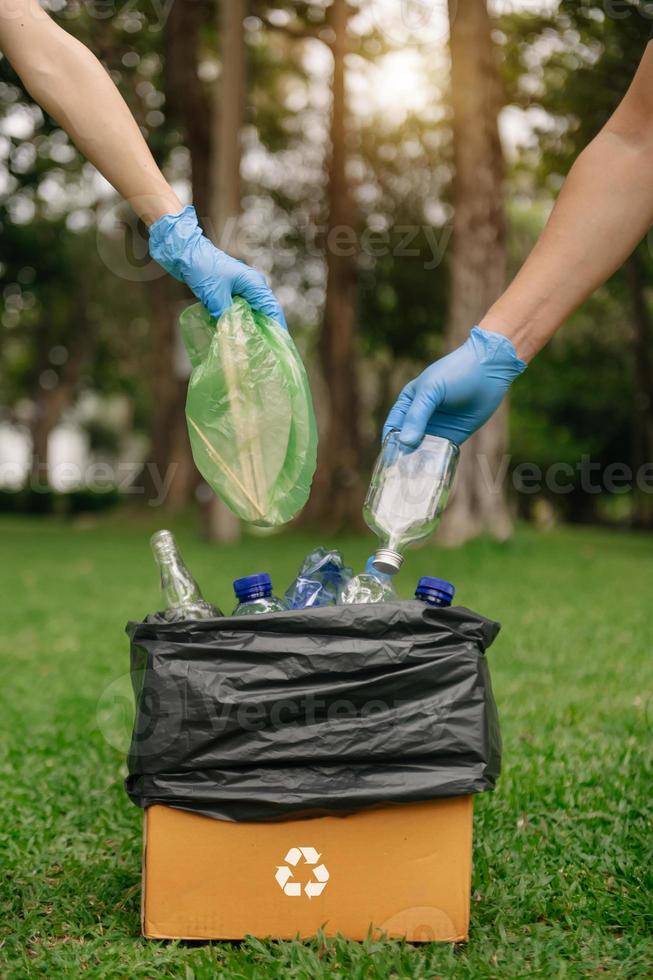 mano de personas sosteniendo botellas de basura de plástico y vidrio poniendo en bolsas de reciclaje. limpieza, contaminación, ecología y concepto. foto