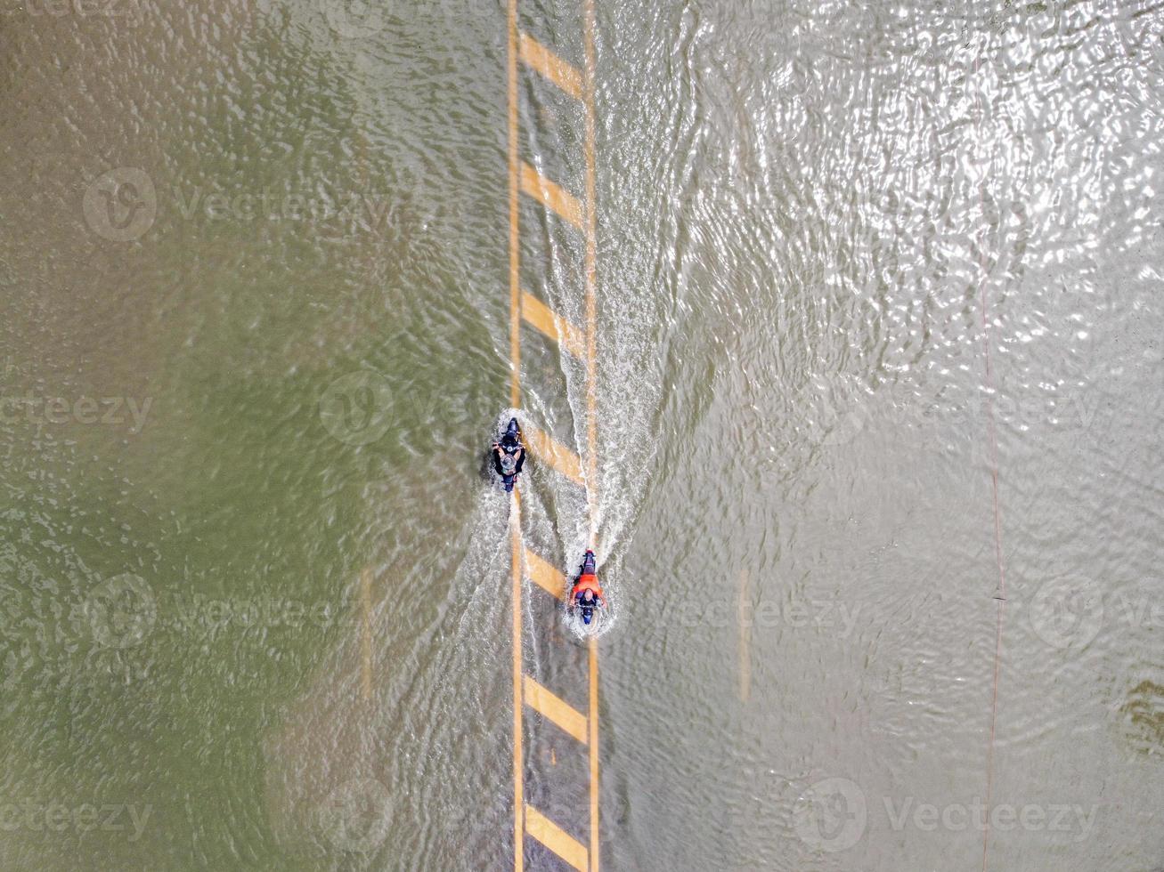 Flooded roads, people with cars running through. Aerial drone photography shows streets flooding and people's cars passing by, splashing water. photo