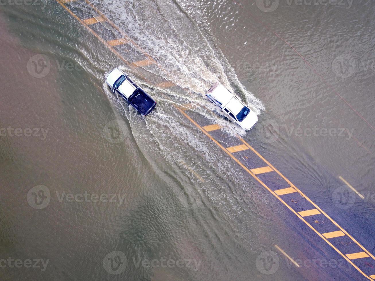 Flooded roads, people with cars running through. Aerial drone photography shows streets flooding and people's cars passing by, splashing water. photo