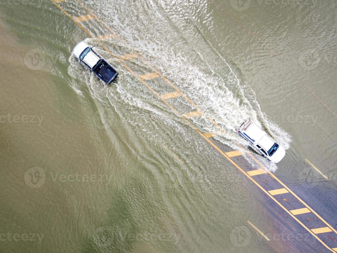 Flooded roads, people with cars running through. Aerial drone photography shows streets flooding and people's cars passing by, splashing water. photo