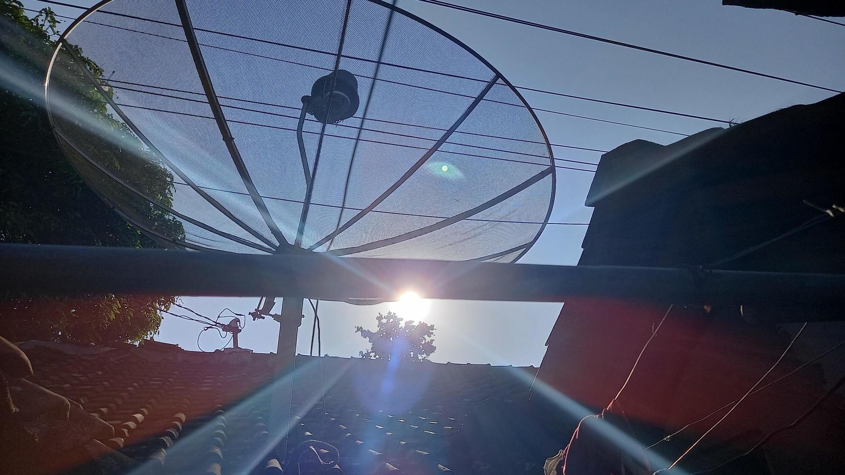 parabolic antenna on top of a roof with sun shining photo