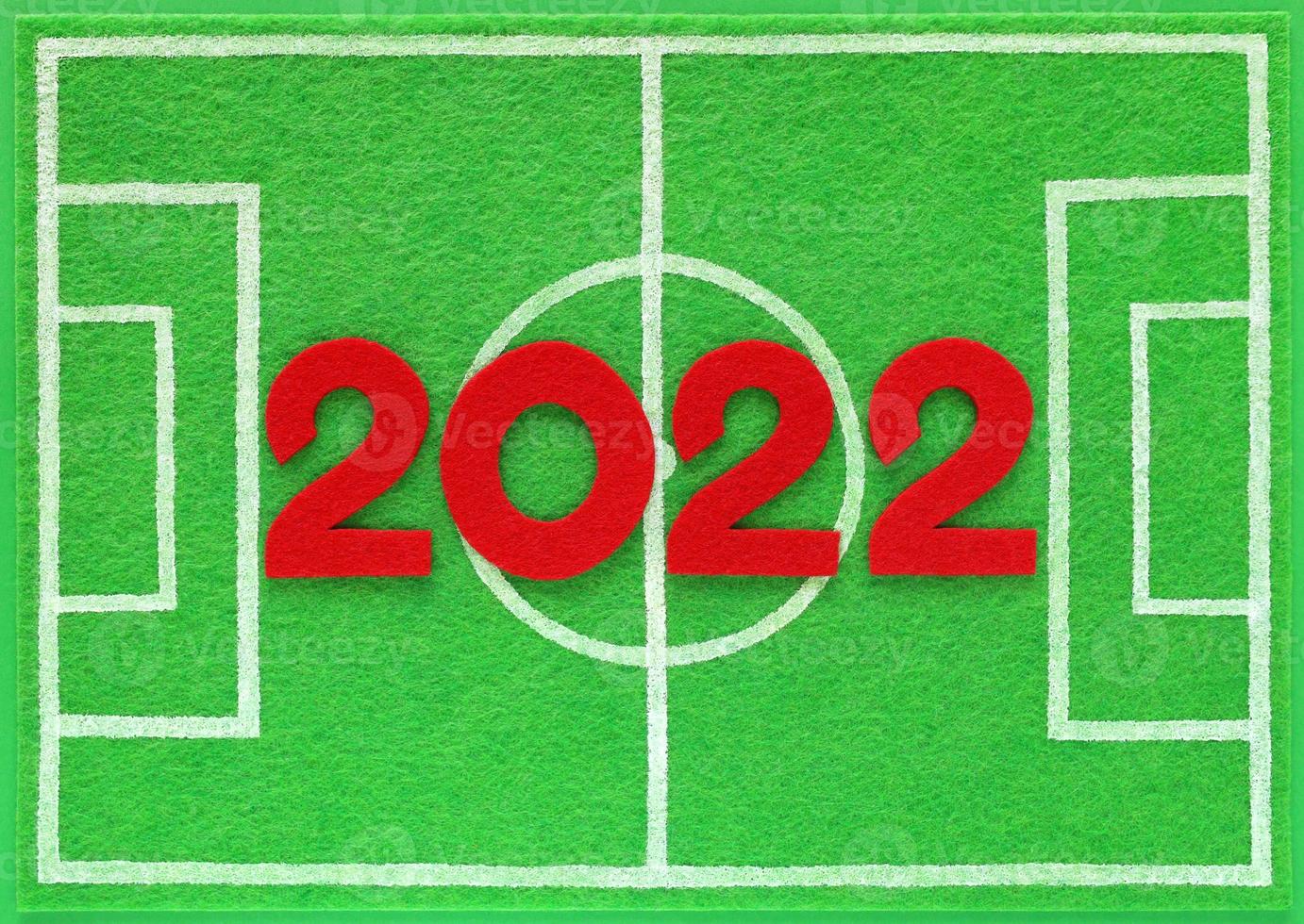 Red felt year numbers 2022 placed on mini football field made of green felt, top view. Concept about schedule of soccer championship matches. Background with copy space. photo