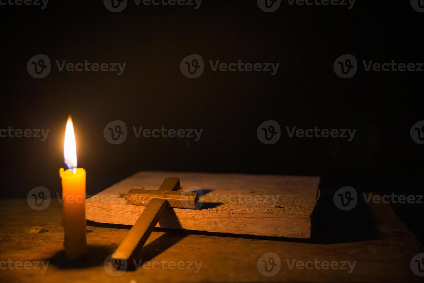 Light candle with holy bible and cross or crucifix on old wooden background in church.Candlelight and open book on vintage wood table christianity study and reading in home.Concept of christ religion photo