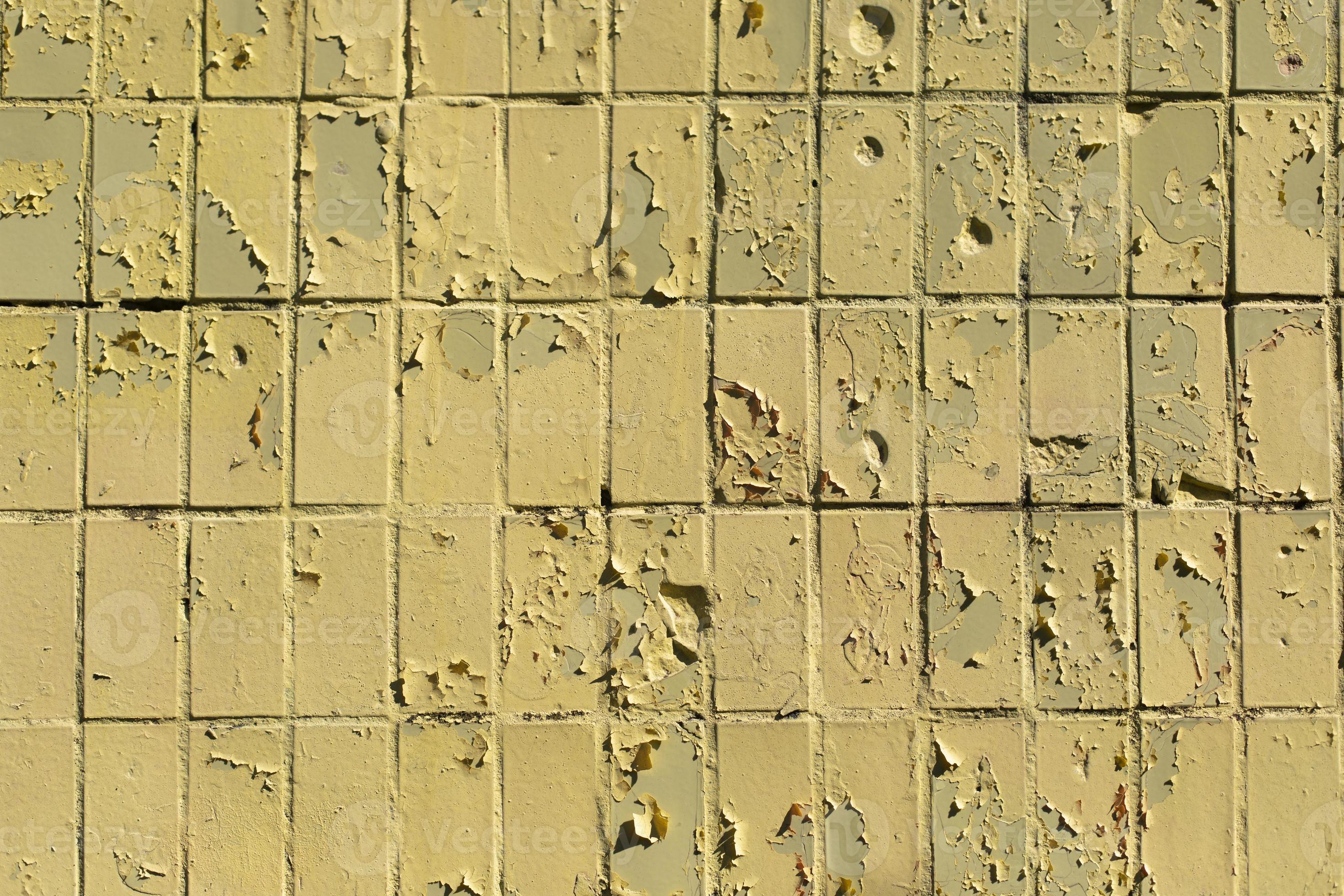 Texture of old tile wall. Yellow paint crumbled. Paint on top of tiles