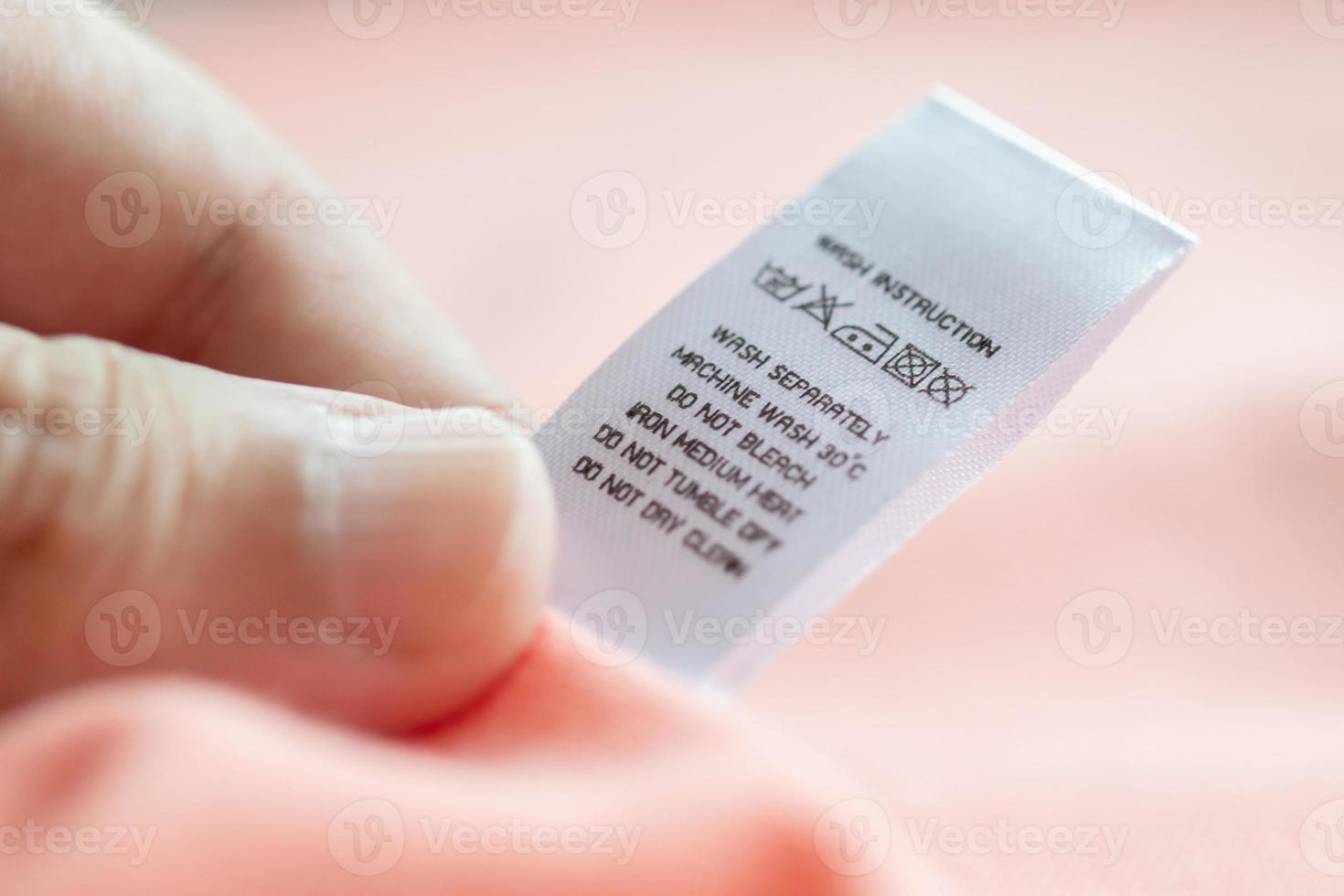 Hand hold and reading at white laundry care washing instructions clothes label on pink shirt photo