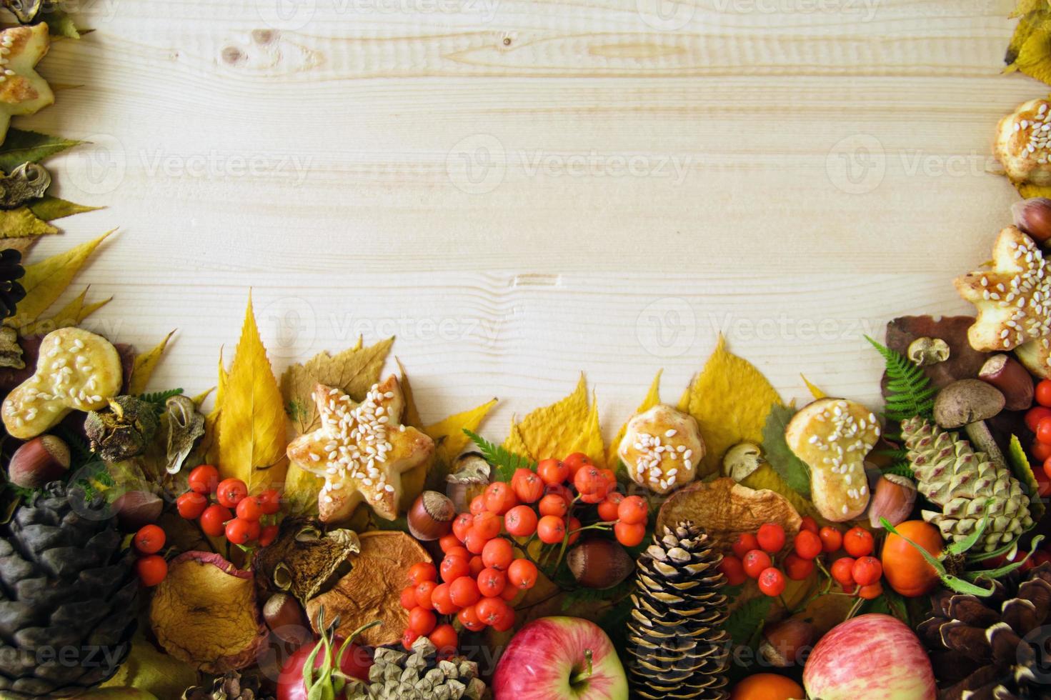 Border from colorful autumn leaves, mushrooms, rose hips, rowanberry, apples, nuts, cones and cookies on the wooden background. Fall background. photo