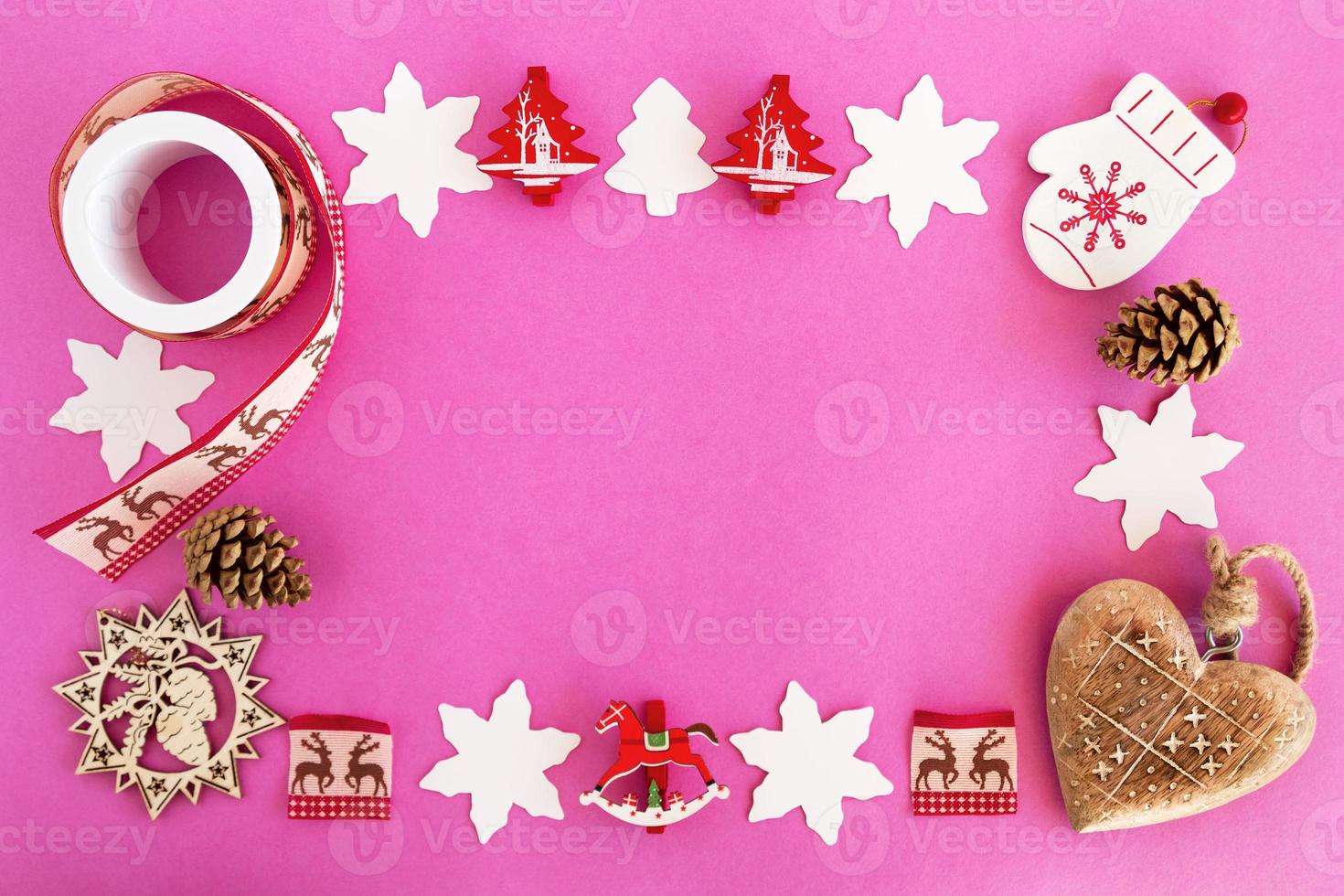 Top view on the frame from red and white wooden Christmas decorations and pine cones on the pink background with copy space. photo