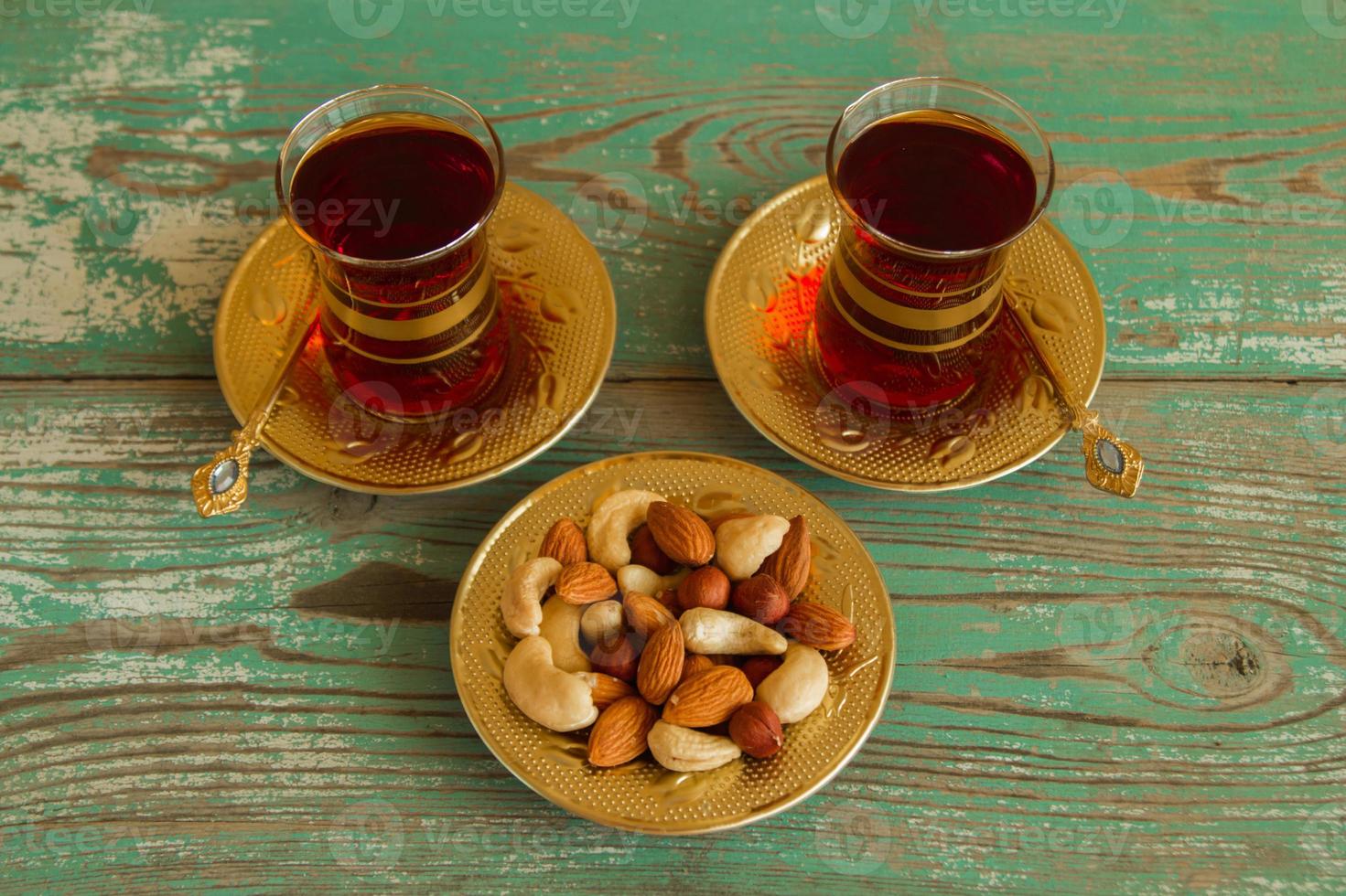Mixed nuts on a yellow metal saucer and two glass cups of Turkish tea on a turquoise wooden background. photo