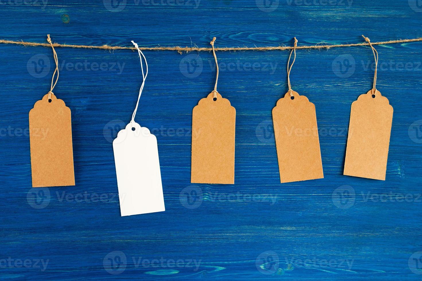 Five brown and white blank paper price tags or labels set hanging on a rope on the blue wooden background. photo