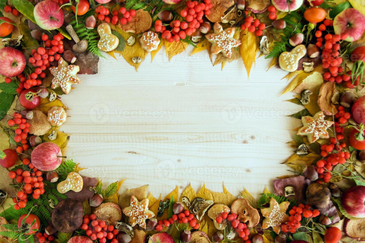 Frame from colorful autumn leaves, mushrooms, rose hips, rowanberry, apples, nuts and cookies on the wooden background. Fall background. photo