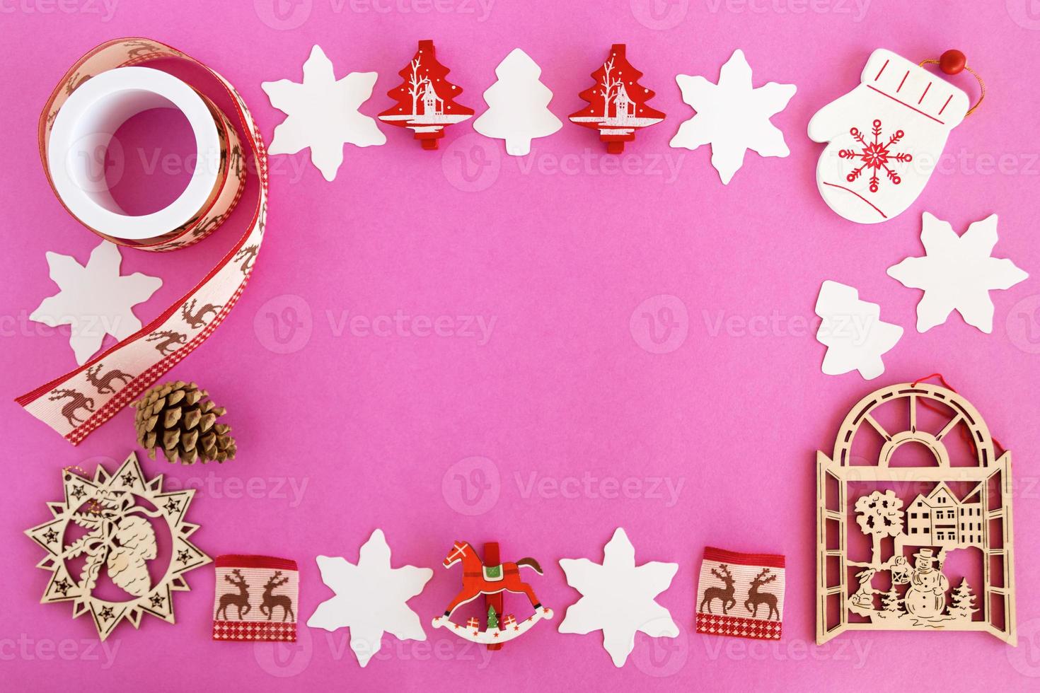 Top view on the frame from red and white wooden Christmas decorations and pine cone on the pink background with copy space. photo