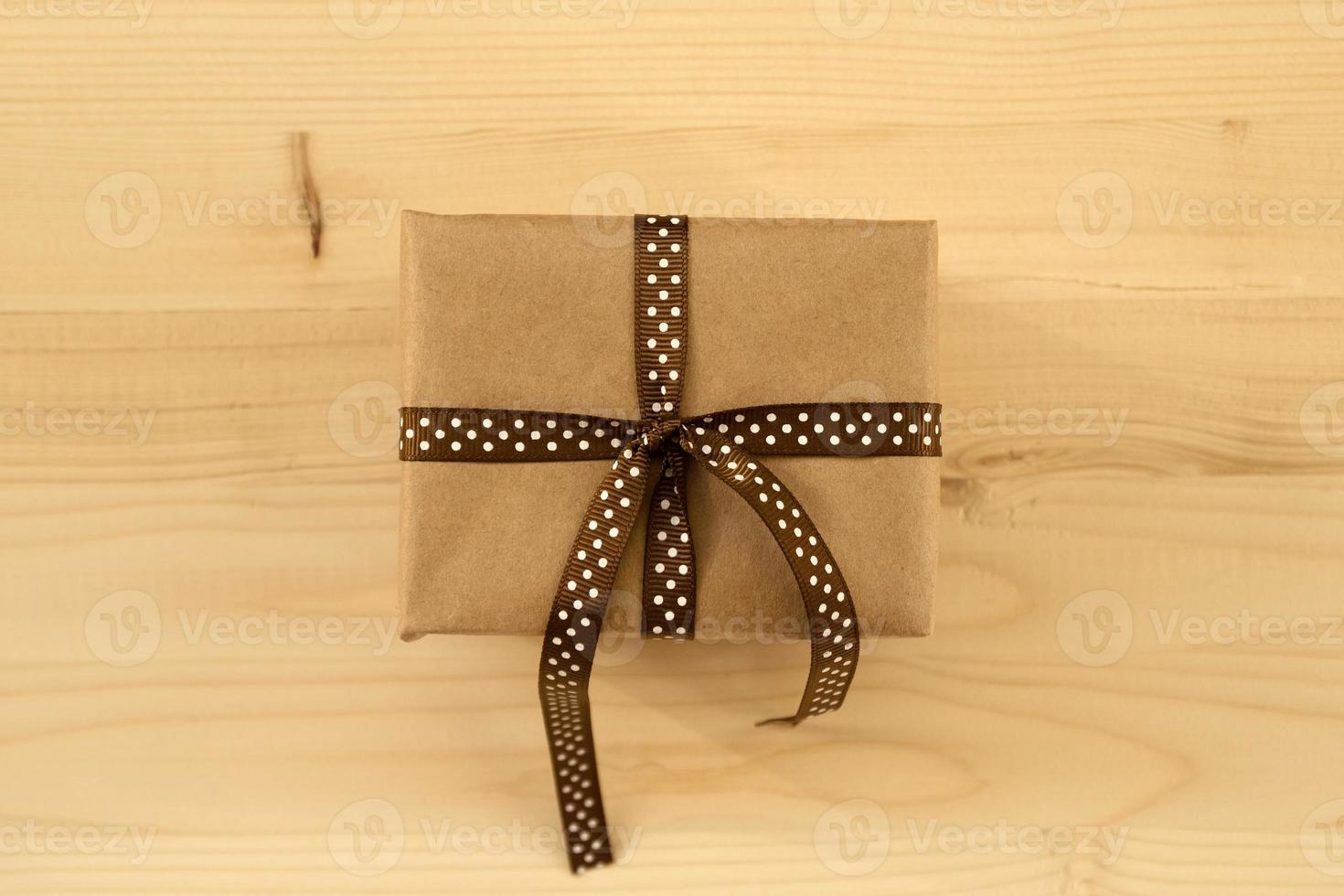 Gift box wrapped of craft paper and brown ribbon on the wooden background, top view. photo