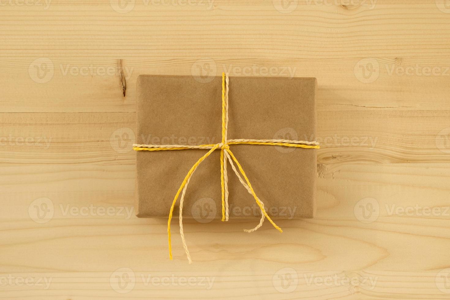 Gift box wrapped of craft paper and white and yellow ribbon on the wooden background, top view. photo