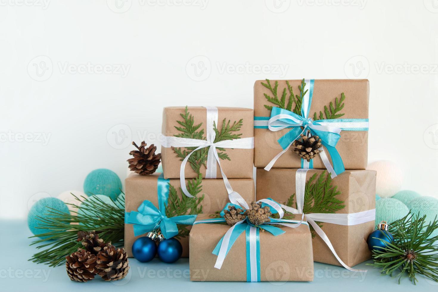 Christmas gift boxes wrapped of craft paper, blue and white ribbons on the blue and white background decorated of pine cones, fir branches, Christmas ball and lights. photo