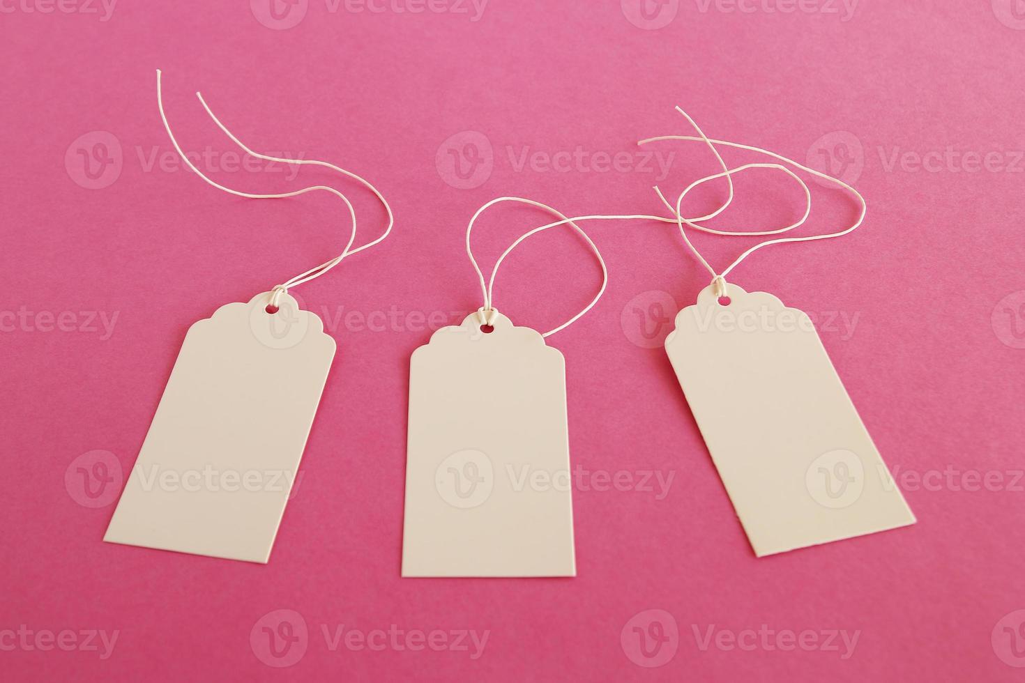 Three white blank paper price tags or labels set on the pink background. photo