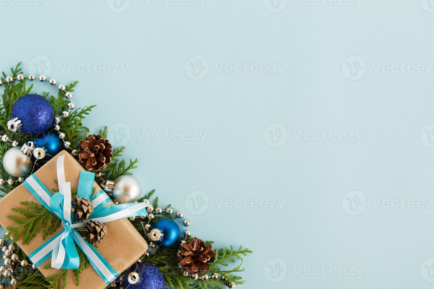 Christmas flat lay composition of fir branches with gift box and decorations at the left bottom corner with copy space on the blue background. photo