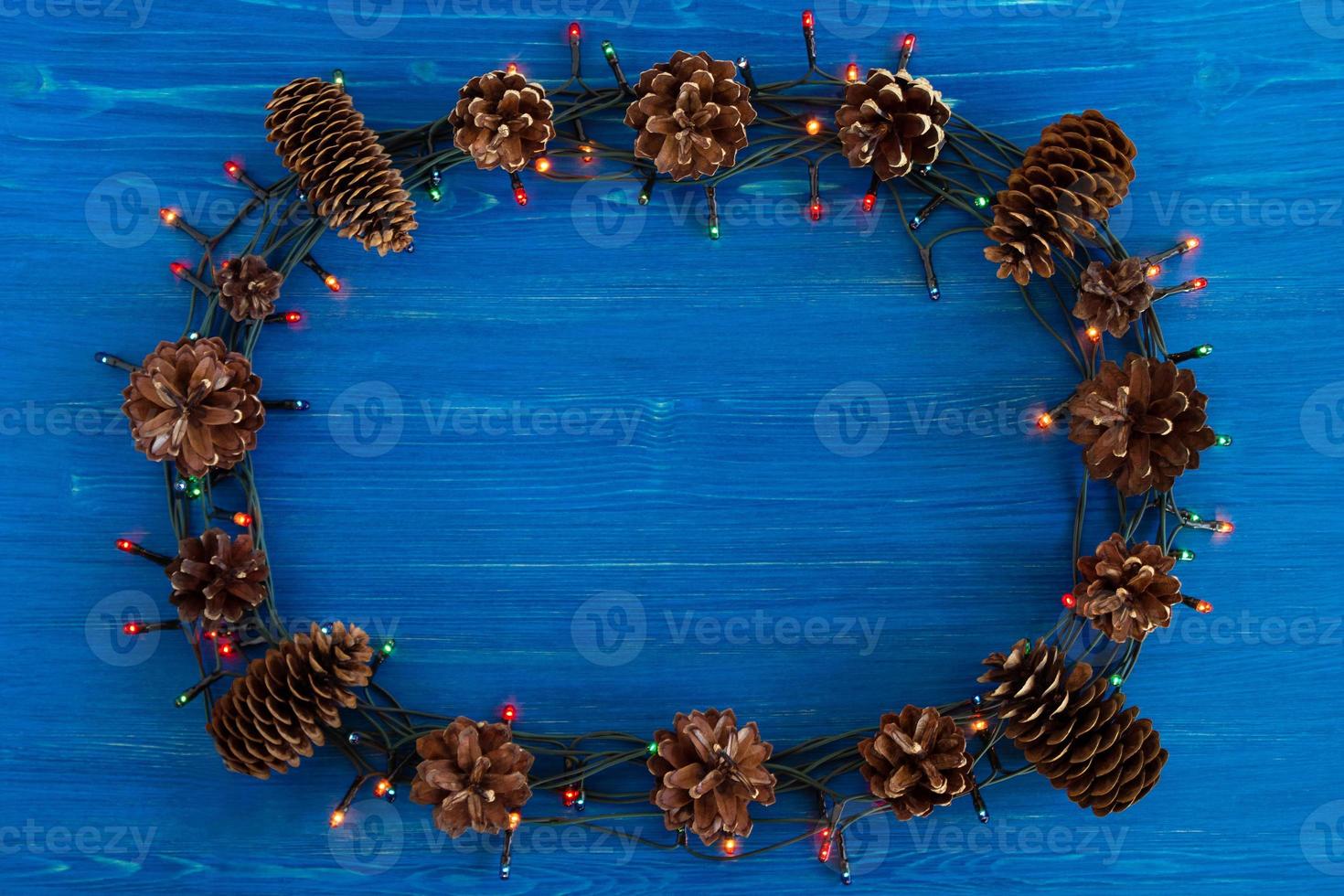 Top view on frame from Christmas lights and pine cones on the blue wooden background with copy space. photo