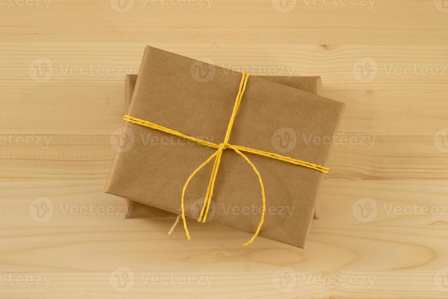 Two gift boxes wrapped of craft paper and yellow ribbon on the wooden background, top view. photo