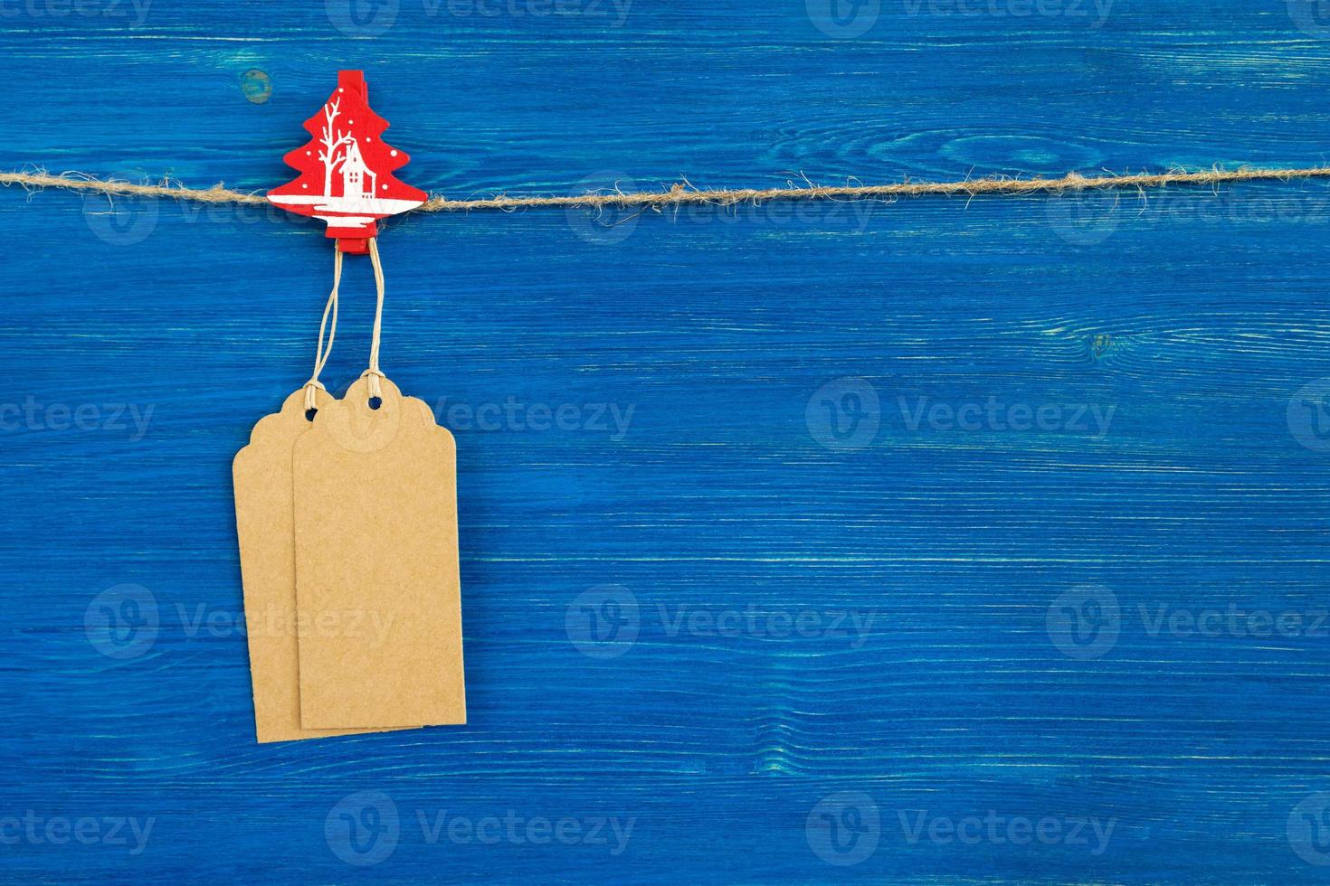 juego de etiquetas o etiquetas de precio de papel en blanco marrón y decoración de madera de navidad colgando de una cuerda en el fondo de madera azul. foto