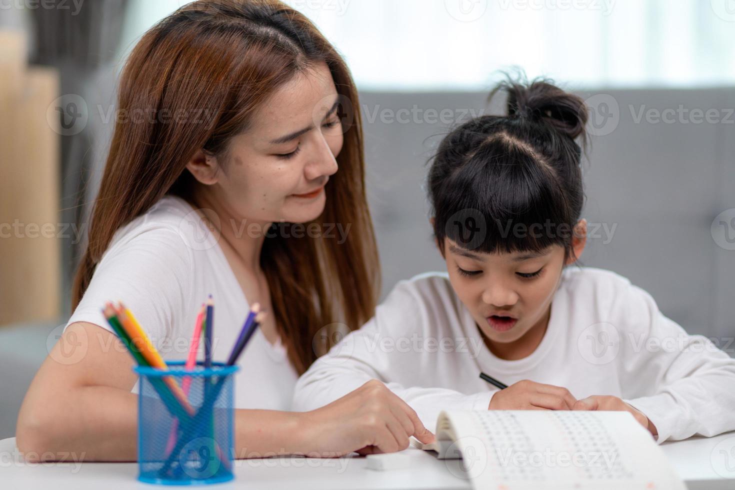 Beautiful Asian woman helping her daughter with homework at home. photo