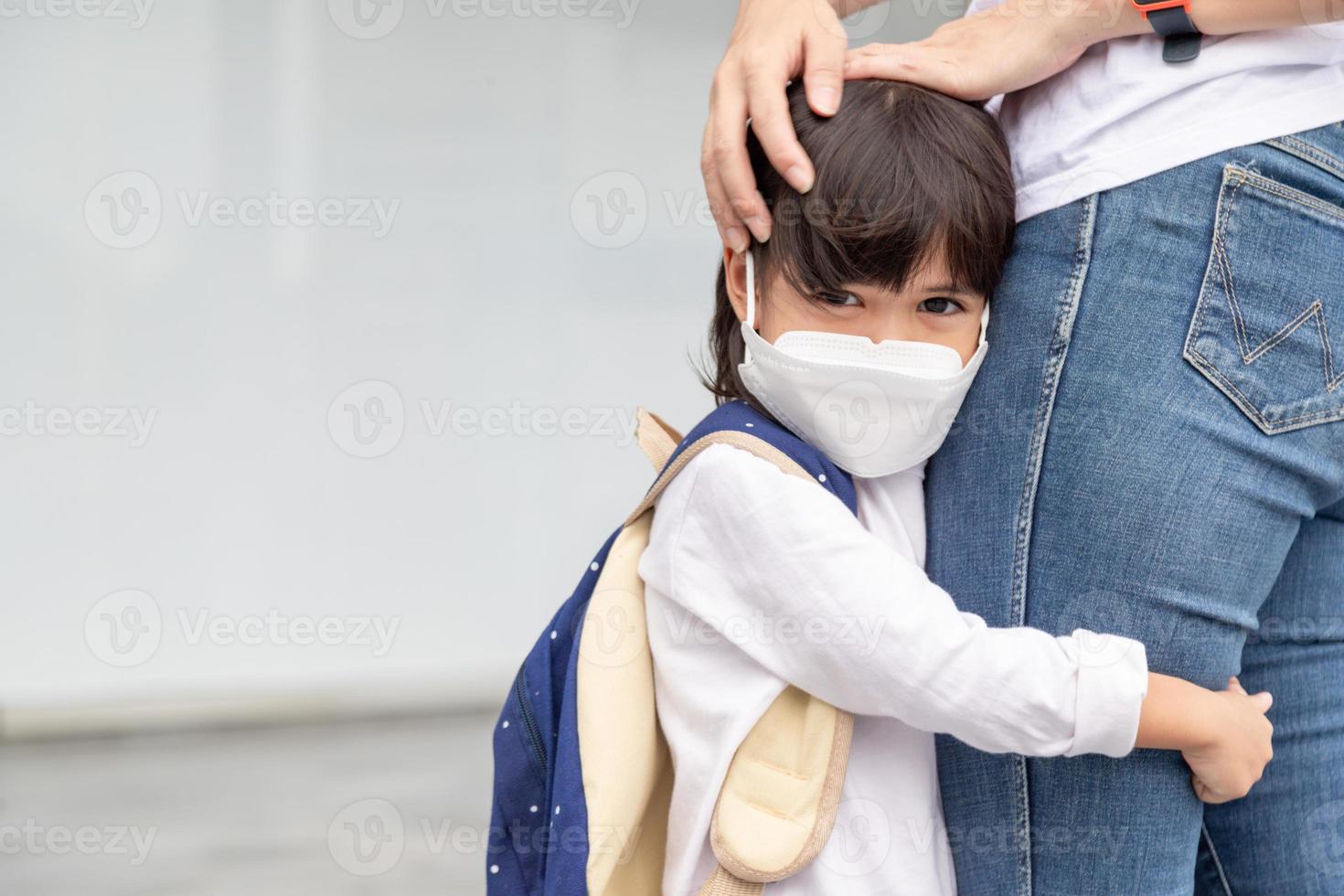 la madre acompaña al niño a la escuela. mamá apoya y motiva al estudiante. la niña con mascarilla no quiere dejar a su madre. teme la escuela primaria. foto